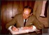 Miguel Delibes Setién escribiendo en un libro de firmas.